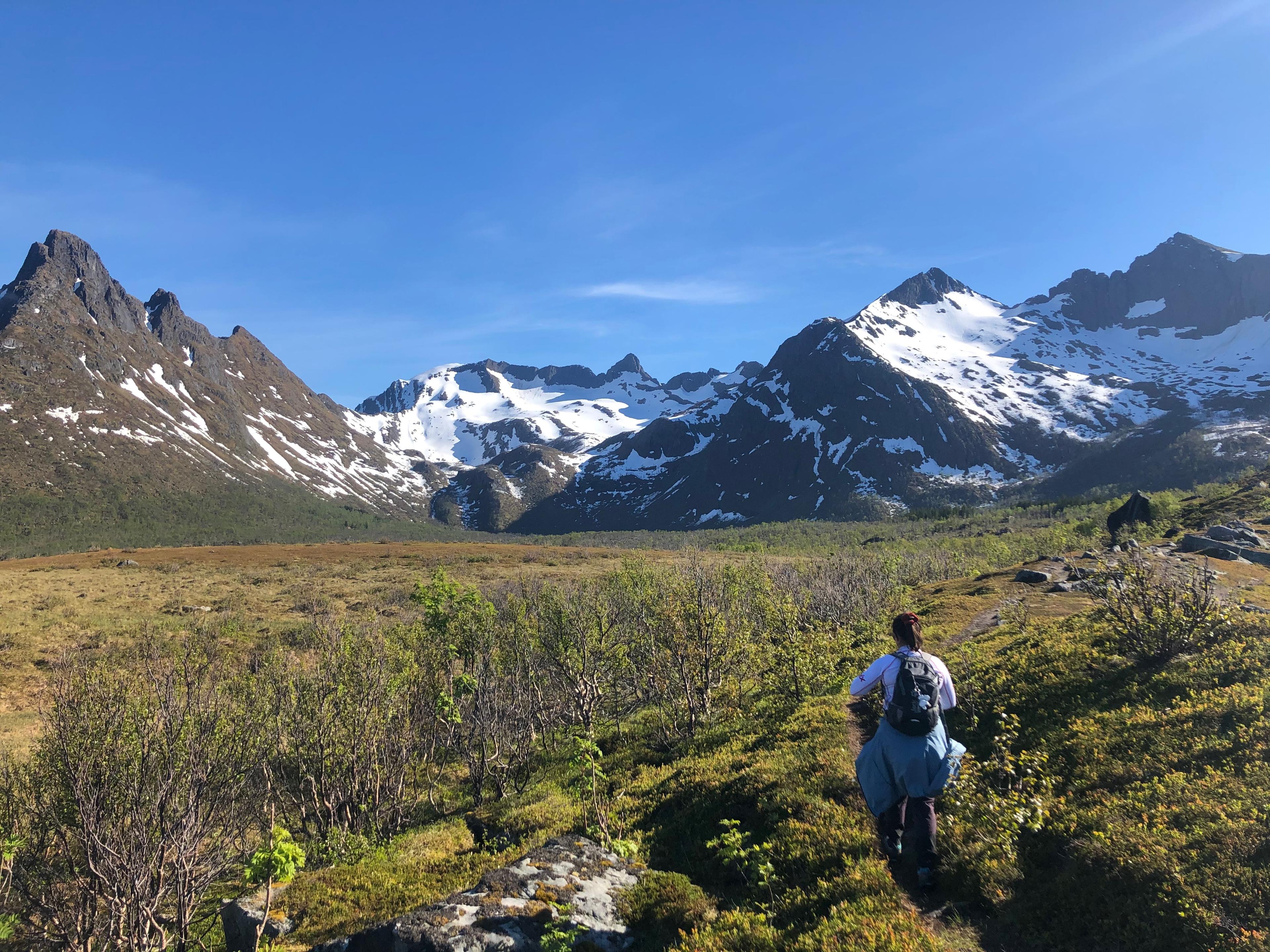 Person på fjelltur mot snødekte tinder en solrik dag